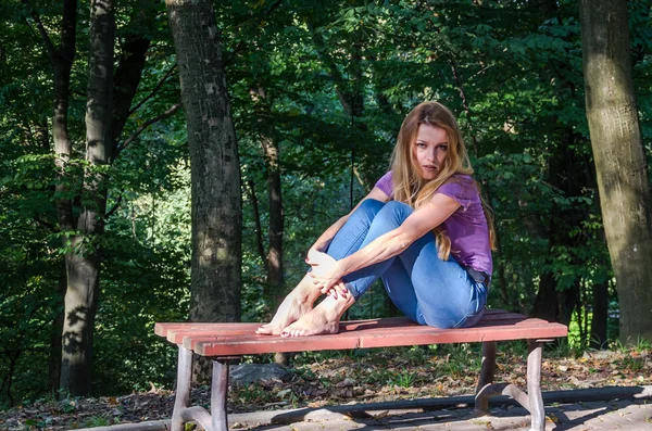 Joven hermosa chica sexy modelo rubio con pelo largo y rubio en jeans y chaqueta posando en el bosque entre los árboles y la vegetación —  Fotos de Stock