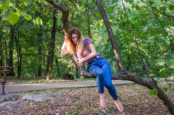 Joven hermosa chica sexy modelo rubio con pelo largo y rubio en jeans y chaqueta posando en el bosque entre los árboles y la vegetación —  Fotos de Stock