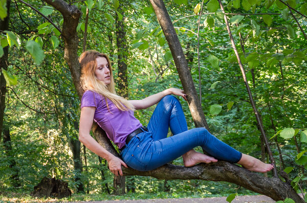 Young beautiful sexy girl blond model with long blond hair in jeans and jacket posing in the woods among the trees and vegetation