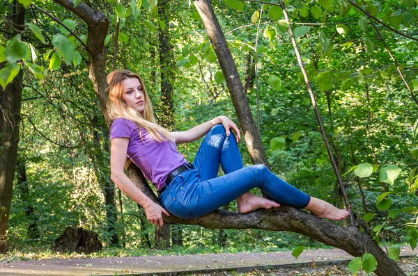 Tânără frumoasă fată sexy model blond cu păr blond lung în blugi și jachetă pozând în pădure printre copaci și vegetație — Fotografie, imagine de stoc
