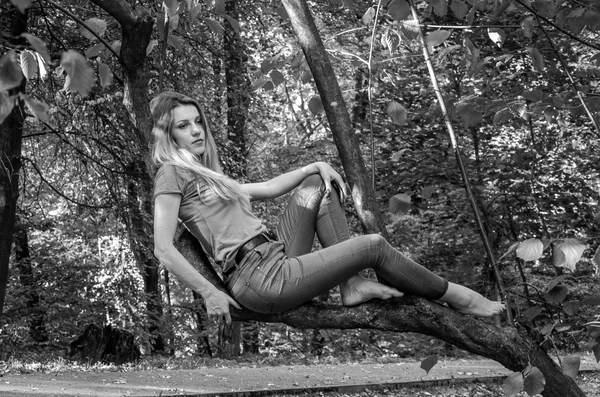 Giovane bella ragazza sexy modello biondo con lunghi capelli biondi in jeans e giacca in posa nel bosco tra gli alberi e la vegetazione — Foto Stock