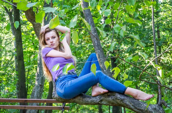 Joven hermosa chica sexy modelo rubio con pelo largo y rubio en jeans y chaqueta posando en el bosque entre los árboles y la vegetación —  Fotos de Stock