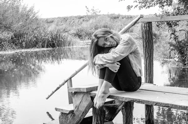 Молода красива жінка модель з довгим світлим волоссям, що сидить з різними емоціями сміх, смуток, смуток, усвідомленість на дерев'яному мосту на березі річки і лісу, шукає воду — стокове фото