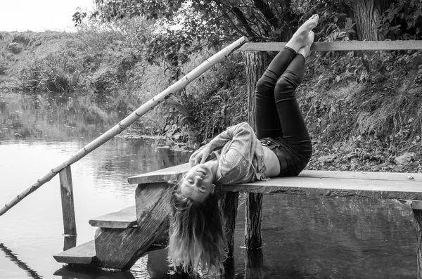 Молода красива жінка модель з довгим світлим волоссям, що сидить з різними емоціями сміх, смуток, смуток, усвідомленість на дерев'яному мосту на березі річки і лісу, шукає воду — стокове фото