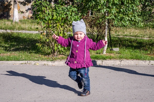 Küçük güzel bir kız bebek ceket, şapka ve gülümseyen ve keyfi mutluluk ilk adımları yapmak yeşil çimenlerin üzerinde yürüyüş parkta oynarken kot — Stok fotoğraf