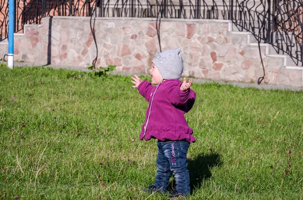 Pequeña niña hermosa abrigo de bebé, sombrero y jeans jugando en el parque caminando sobre hierba verde haciendo sus primeros pasos sonriendo y disfrutando de la felicidad — Foto de Stock