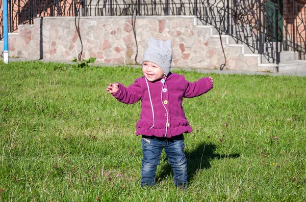 Pequeña niña hermosa abrigo de bebé, sombrero y jeans jugando en el parque caminando sobre hierba verde haciendo sus primeros pasos sonriendo y disfrutando de la felicidad — Foto de Stock