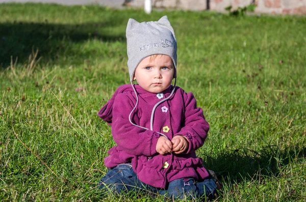 Fetiță frumoasă haină pentru copii, pălărie și blugi care se joacă în parc mergând pe iarbă verde făcând primii pași zâmbind și bucurându-se de fericire — Fotografie, imagine de stoc