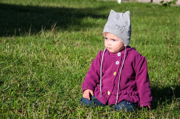 Gadis kecil yang cantik mantel bayi, topi dan jeans bermain di taman berjalan di rumput hijau melakukan langkah pertama mereka tersenyum dan menikmati kebahagiaan — Stok Foto