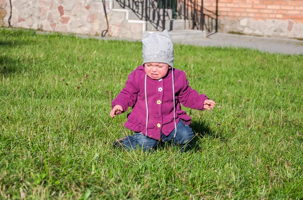 Bambina bella cappotto bambino, cappello e jeans che giocano nel parco camminando su erba verde facendo i loro primi passi sorridendo e godendo la felicità — Foto Stock