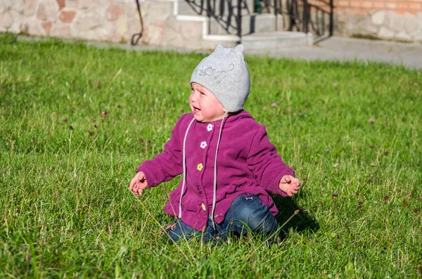 Mooi meisje baby jas, muts en jeans spelen in het park wandelen op groen gras doen hun eerste stappen glimlachend en genieten van geluk — Stockfoto