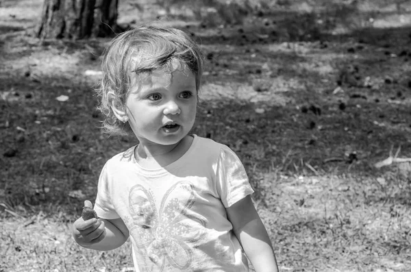 Kleine mooie babymeisje in een wit T-shirt met een geschilderde bloem, wandelen en spelen in het bos tussen de bomen en struiken, Eet smakelijk, Rode aardbei — Stockfoto