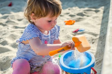Küçük sevimli kız bebek oyun alanında kova kum kum Höyük üzerinde bir kürek ve Komisyon ile oyun