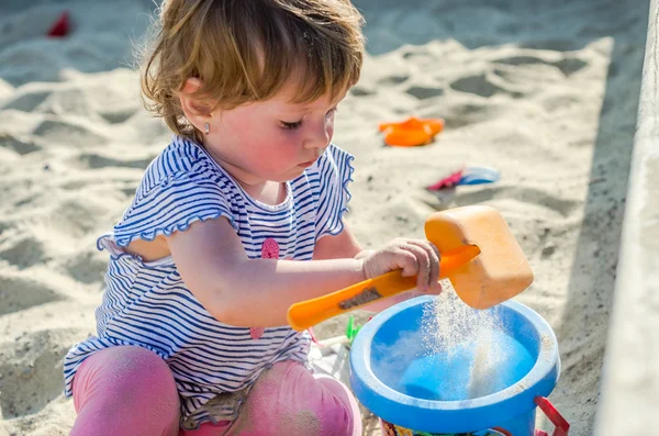 Küçük sevimli kız bebek oyun alanında kova kum kum Höyük üzerinde bir kürek ve Komisyon ile oyun