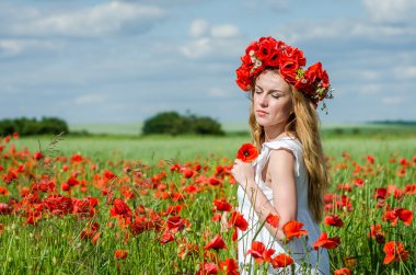 Kafasında bir çelenk ile haşhaş alanındaki beyaz elbiseli uzun saçlı genç güzel mutlu kız