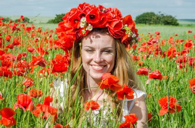 Kafasında bir çelenk ile haşhaş alanındaki beyaz elbiseli uzun saçlı genç güzel mutlu kız