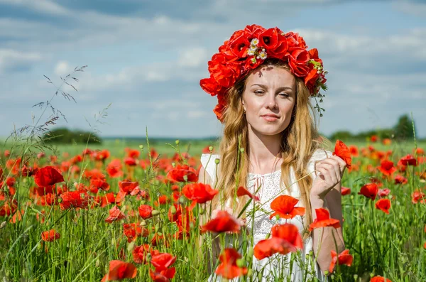 Menina feliz bonita nova com cabelo longo em um vestido branco no campo da papoula com uma grinalda em sua cabeça — Fotografia de Stock