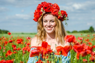 Kafasında bir çelenk ile haşhaş alanındaki beyaz elbiseli uzun saçlı genç güzel mutlu kız