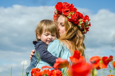 Uzun saçlı, çekici bir kadın. Kızı kollarında bir buket haşhaş çelengiyle gelincik tarlasında yürüyen bir anne.