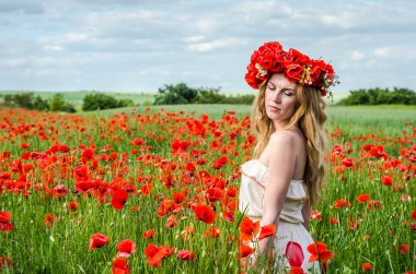 Kafasında bir çelenk ile haşhaş alanındaki beyaz elbiseli uzun saçlı genç güzel mutlu kız