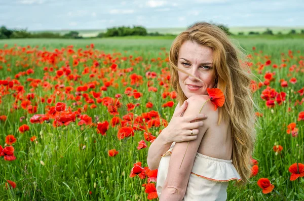 Charming beautiful sexy girl with long hair and gorgeous makeup walks on a poppy field holding a bouquet of red poppies — Stock Photo, Image