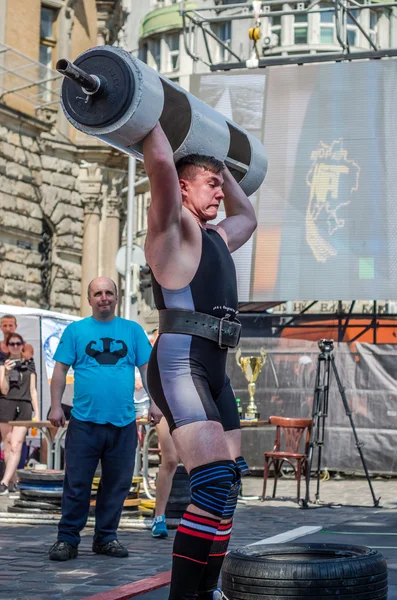 LVIV, UCRANIA - JUNIO 2016: Un hombre fuerte en la forma deportiva culturista levanta una pesada barra en la calle — Foto de Stock