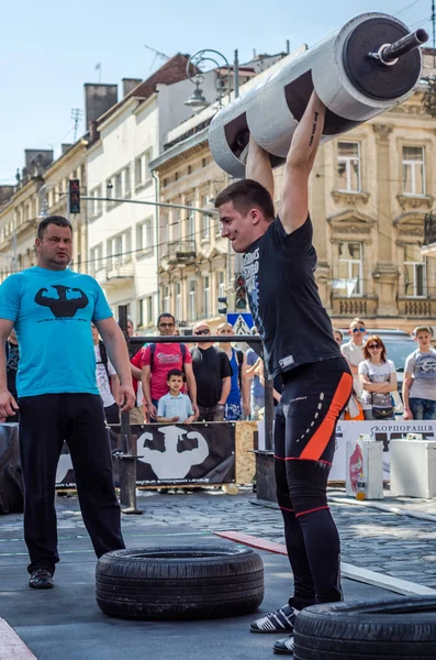 LVIV, UCRANIA - JUNIO 2016: Un hombre fuerte en la forma deportiva culturista levanta una pesada barra en la calle — Foto de Stock