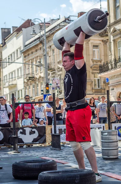 LVIV, UCRANIA - JUNIO 2016: Un hombre fuerte en la forma deportiva culturista levanta una pesada barra en la calle — Foto de Stock