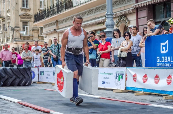 LVIV, UCRANIA - JUNIO 2016: Strongman con un gran cuerpo de metal inflado lleva maletas pesadas — Foto de Stock