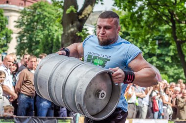 LVIV, UKRAINE - JUNE 2016: Athlete bodybuilder strongman with strong body has an enormous metal barrel with beer clipart