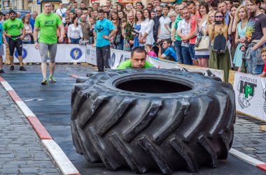Lviv, Ukrayna - Haziran 2016: Atlet vücut geliştirmeci diktatör güçlü gövdeli bir büyük bir kamyon lastik tekerlek dönme iter