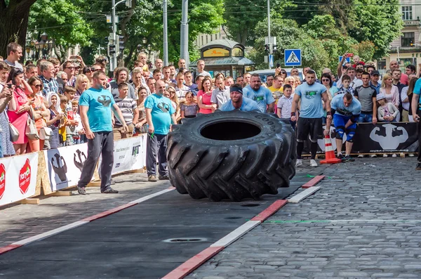 LVIV, UCRANIA - JUNIO 2016: atleta culturista fuerte con el cuerpo fuerte empuja un enorme girar la rueda de un neumático de camión — Foto de Stock