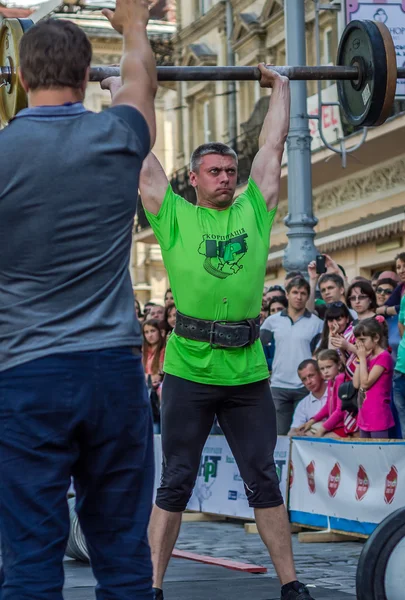 LVIV, UCRANIA - JUNIO 2016: Fuerte atleta culturista fuerte levanta una pesada barra delante de la audiencia en una calle de la ciudad — Foto de Stock