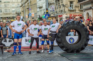 Lviv, Ukrayna - Haziran 2016: Güçlü vücut geliştirmeci atlet, atlet şaşkın kamu önünde sokakta kamyondan büyük bir siyah Goodyear tekerleği rulo