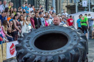 Lviv, Ukrayna - Haziran 2016: Güçlü vücut geliştirmeci atlet, atlet şaşkın kamu önünde sokakta kamyondan büyük bir siyah Goodyear tekerleği rulo