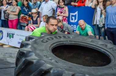 Lviv, Ukrayna - Haziran 2016: Güçlü vücut geliştirmeci atlet, atlet şaşkın kamu önünde sokakta kamyondan büyük bir siyah Goodyear tekerleği rulo