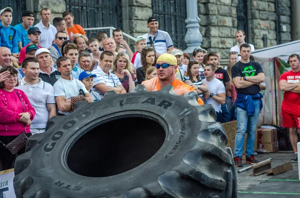 Lviv, Ukrayna - Haziran 2016: Güçlü vücut geliştirmeci atlet, atlet şaşkın kamu önünde sokakta kamyondan büyük bir siyah Goodyear tekerleği rulo