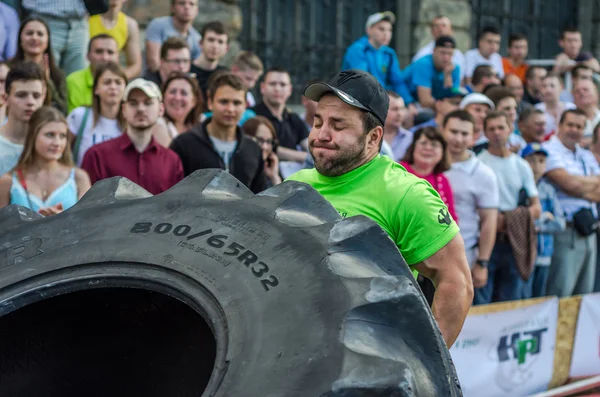 Lviv, Ukrayna - Haziran 2016: Güçlü vücut geliştirmeci atlet, atlet şaşkın kamu önünde sokakta kamyondan büyük bir siyah Goodyear tekerleği rulo