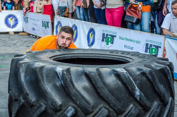 LVIV, UCRANIA - JUNIO 2016: Fuerte culturista atleta, el atleta rueda la rueda de un enorme Goodyear negro desde el camión en la calle frente al público asombrado — Foto de Stock