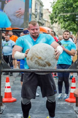 Lviv, Ukrayna - Haziran 2016: Güçlü vücut geliştirmeci strongman mermerden yapılmış büyük bir ağır taş topu kaldırır ve şaşkın seyircilerin gözleri altında sokakta bar üzerine atar