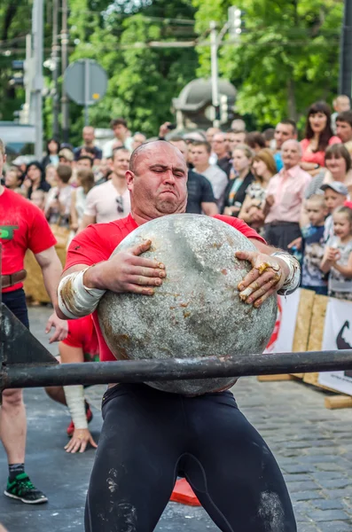 LVIV, UKRAINE - JUNE 2016: Strong bodybuilder strongman lifts a huge heavy stone ball made of marble and throws it over the bar on the street under the eyes of stunned spectators