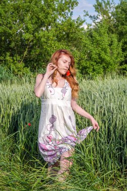 Seksi bacak açığa beyaz bir sundress güzel, seksi kırmızı çiçek haşhaş ağzına, ile arasında buğday spikelets alanındaki yürüme genç sevimli kız