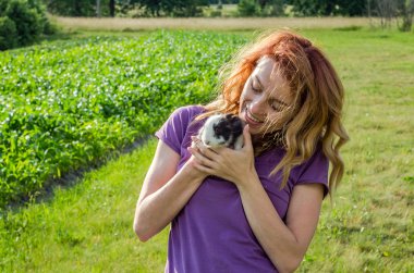 Genç güzel kadın çiftçi onun bahçesinde bir köyde bir gömlek uzun saçlı iki genç tüylü tavşan, gülümseyerek elele yürüyor ve mutluluk ile yeni yavrular sevinir