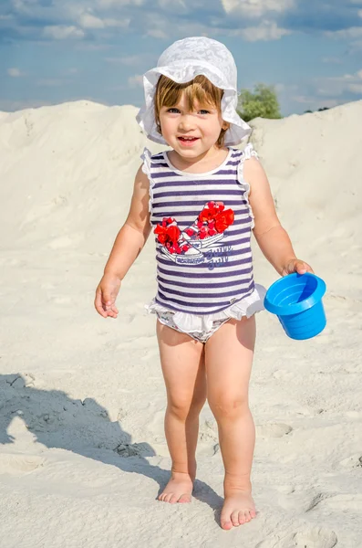 Mała dziewczynka słodkie dziecko bawiące się w piasku w T-shirt, szorty i kapelusz na piaszczystej plaży na jasne upalny słoneczny dzień na plaży w ośrodku — Zdjęcie stockowe
