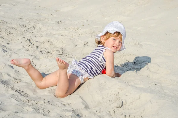 Mała dziewczynka słodkie dziecko bawiące się w piasku w T-shirt, szorty i kapelusz na piaszczystej plaży na jasne upalny słoneczny dzień na plaży w ośrodku — Zdjęcie stockowe