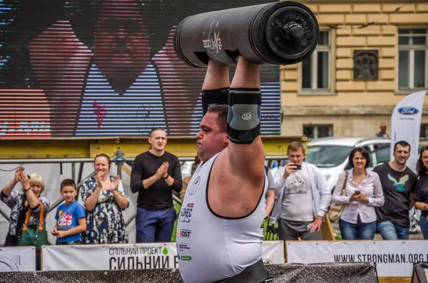 LVIV, UKRAINE - JULY 2016: Strong athlete bodybuilder pumped strongman with a heavy body raises the bar in front of a pack of enthusiastic spectators on the street on a sunny day