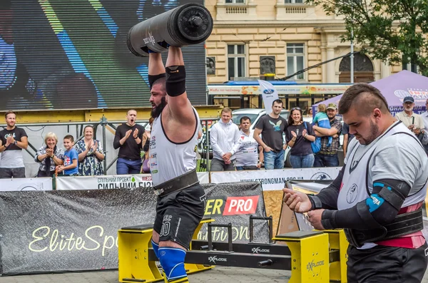 LVIV, UCRANIA - JULIO 2016: Fuerte culturista atleta bombeado hombre fuerte con un cuerpo pesado eleva la barra delante de un grupo de espectadores entusiastas en la calle en un día soleado — Foto de Stock