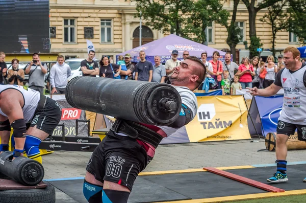 LVIV, UCRANIA - JULIO 2016: Fuerte culturista atleta bombeado hombre fuerte con un cuerpo pesado eleva la barra delante de un grupo de espectadores entusiastas en la calle en un día soleado — Foto de Stock