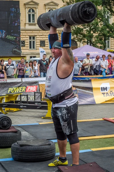 LVIV, UCRANIA - JULIO 2016: Fuerte culturista atleta bombeado hombre fuerte con un cuerpo pesado eleva la barra delante de un grupo de espectadores entusiastas en la calle en un día soleado — Foto de Stock