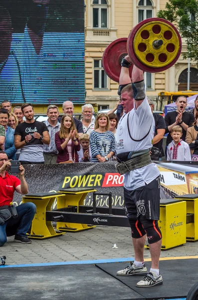 LVIV, UCRANIA - JULIO 2016: Fuerte culturista atleta bombeado hombre fuerte con un cuerpo pesado eleva la barra delante de un grupo de espectadores entusiastas en la calle en un día soleado — Foto de Stock